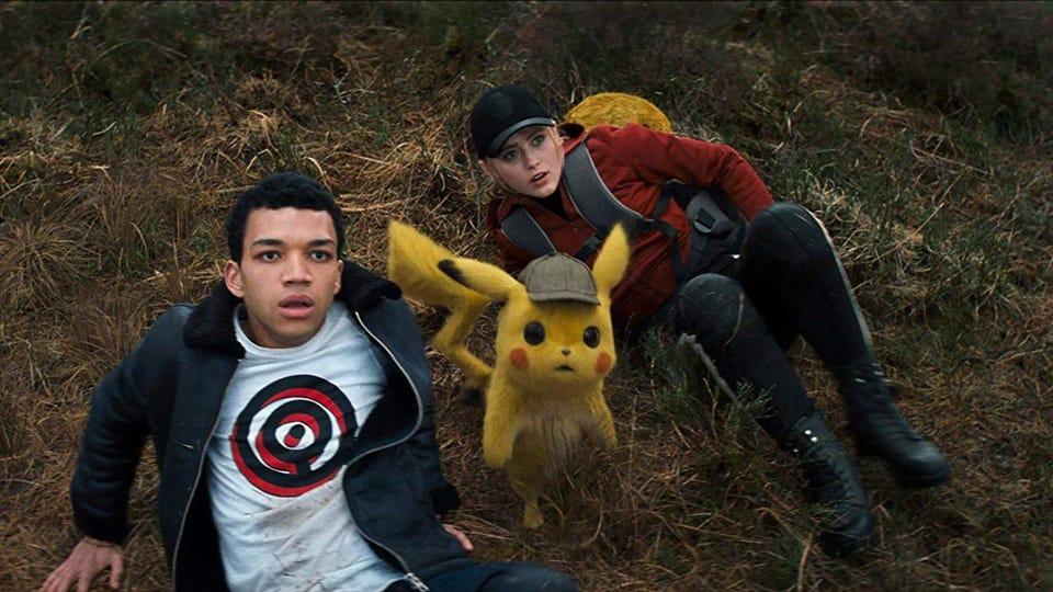 A still from the motion picture "Pokemon : Detective Pikachu". Tom (Justice Smith), Pikachu, and Kathryn (Lucy Stevens) are on the ground, looking up towards the camera.