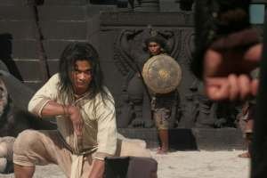 A man kneels down in a fighting stance before soldiers in a still from Ong Bak 3