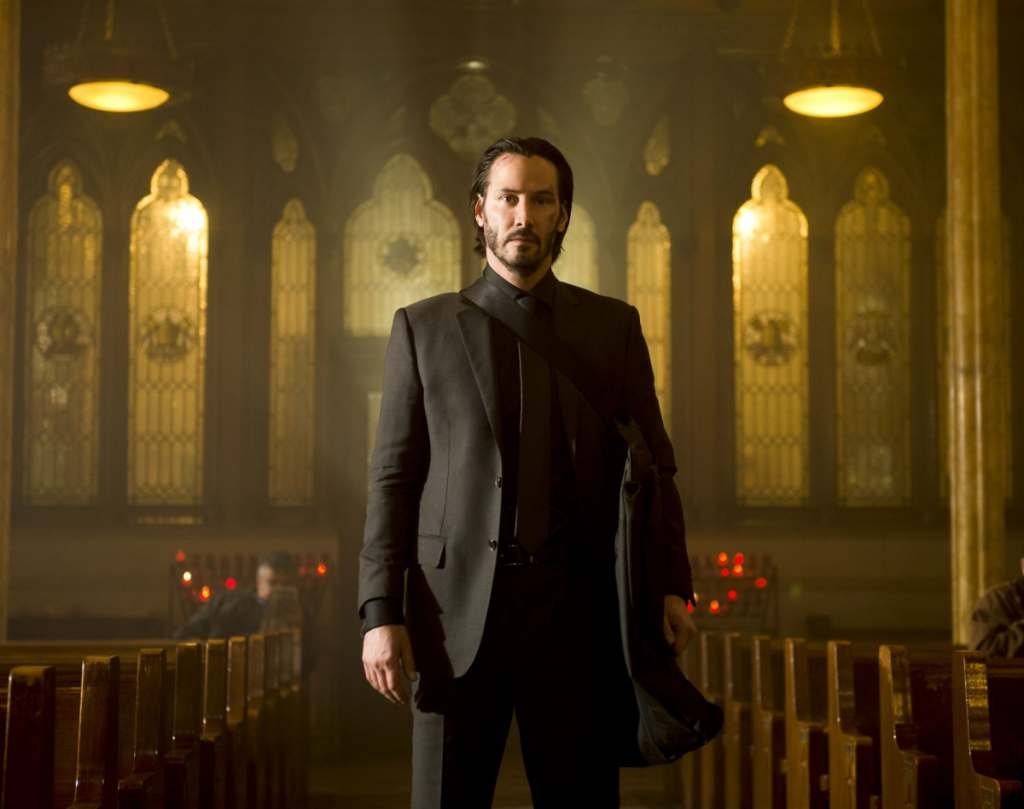 A man in a black suit standing center-aisle in a church.