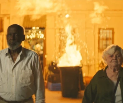 A man and a woman stand in front of an explosion.