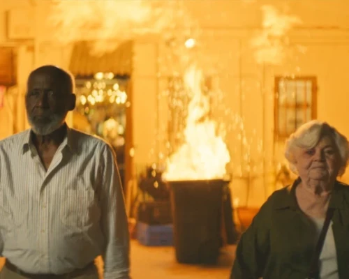 A man and a woman stand in front of an explosion.