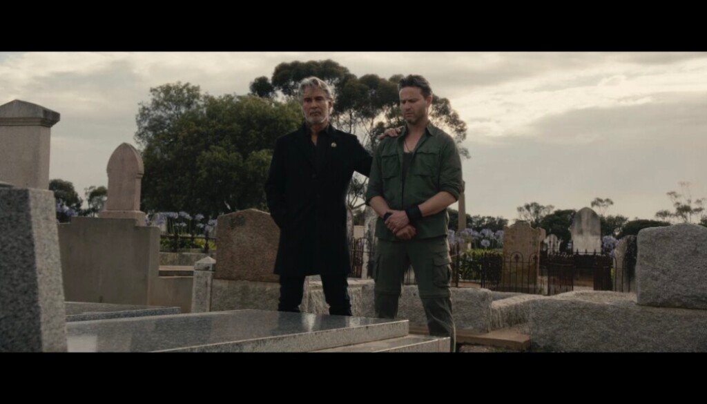 Two men stand side by side over a grave.