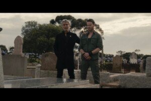 Two men stand side by side over a grave.