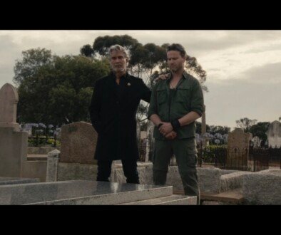 Two men stand side by side over a grave.