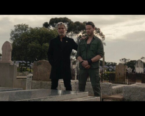 Two men stand side by side over a grave.