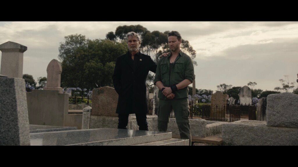 Two men stand side by side over a grave.
